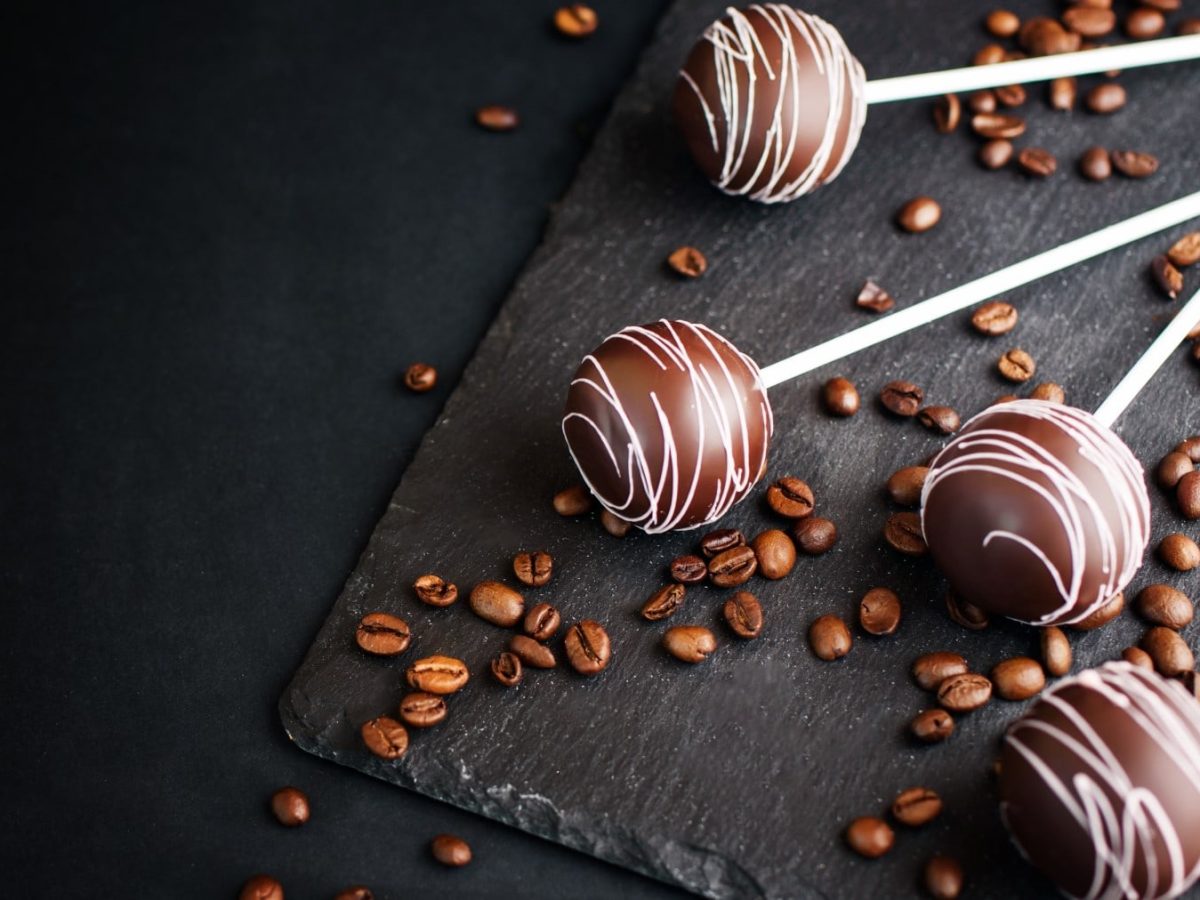 Mehrere Kaffe Cake Pops neben Kaffeebohnen vor schwarzem Hintergrund.