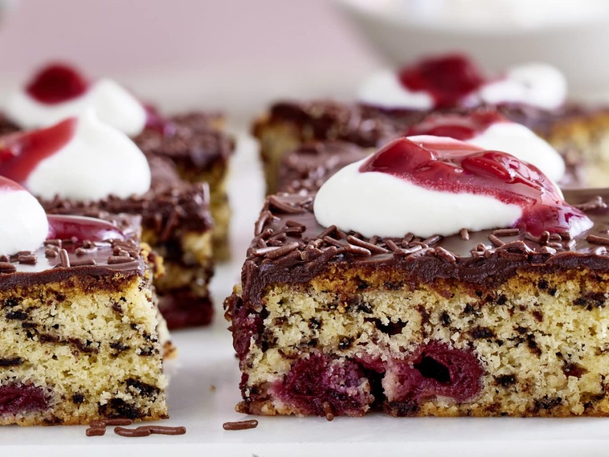 Kirsch-Ameisenkuchen in Stücken garniert mit Sahne und Kirschgrütze vor hellem Hintergrund.