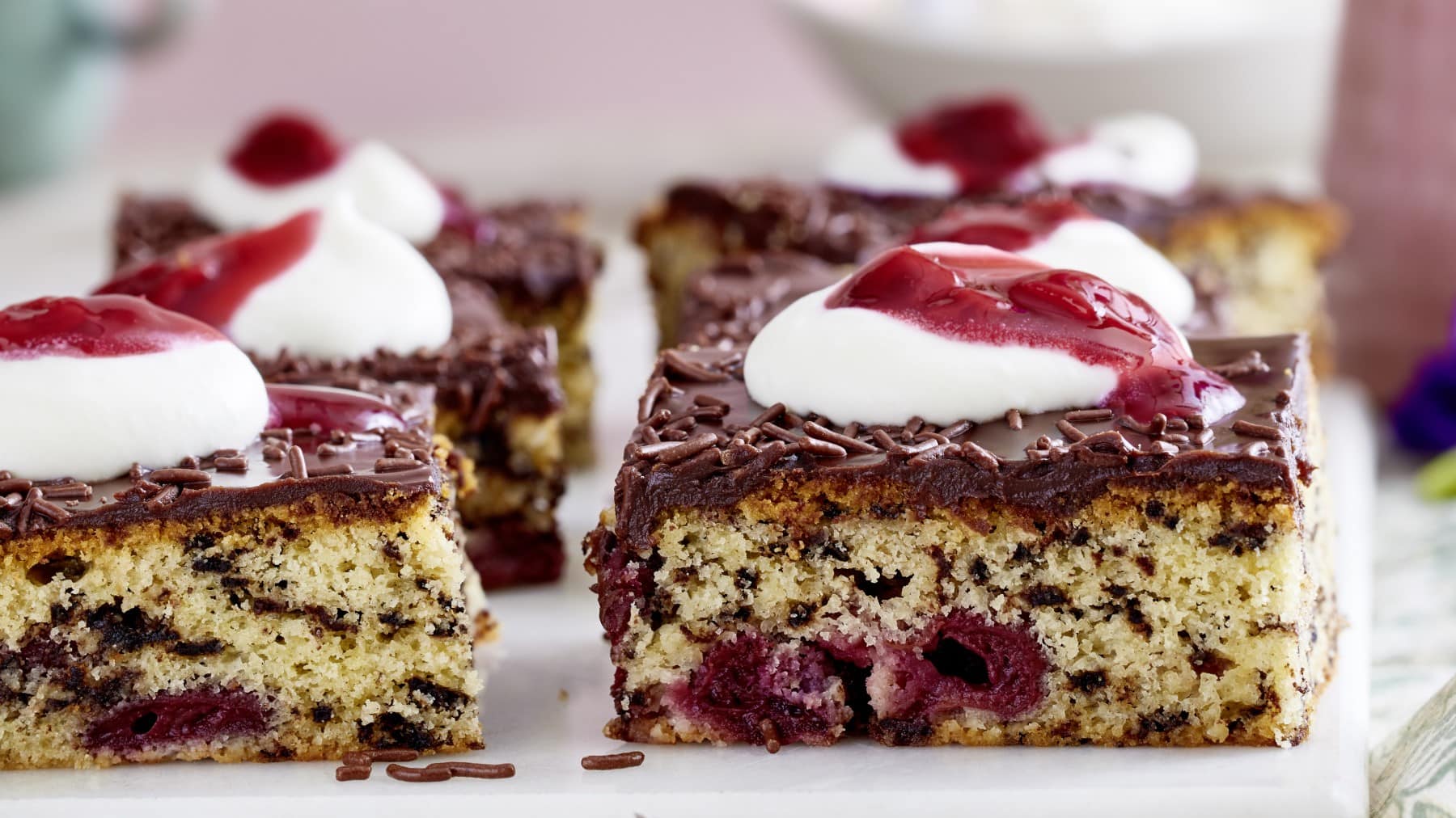 Kirsch-Ameisenkuchen in Stücken garniert mit Sahne und Kirschgrütze vor hellem Hintergrund.