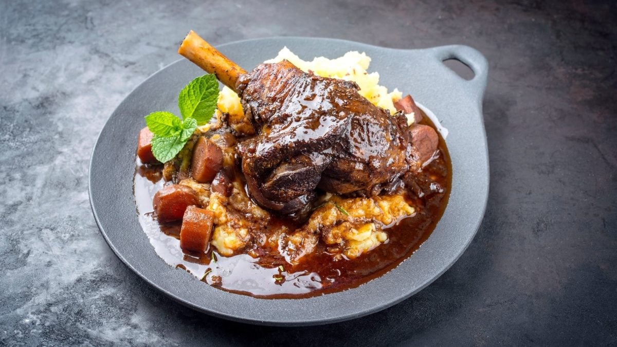 Ein grauer Teller mit der Lammkeule, KArtoffelpüree und Sauce auf einem dunklen Untergrund.