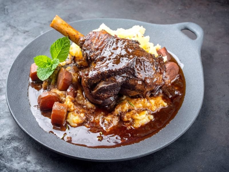 Ein grauer Teller mit der Lammkeule, KArtoffelpüree und Sauce auf einem dunklen Untergrund.