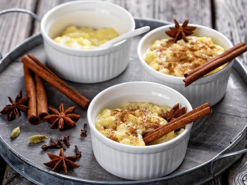 Drei Schalen Lebkuchen-Milchreis mit Zimtstangen, Sternanis und Zimt-Zucker.