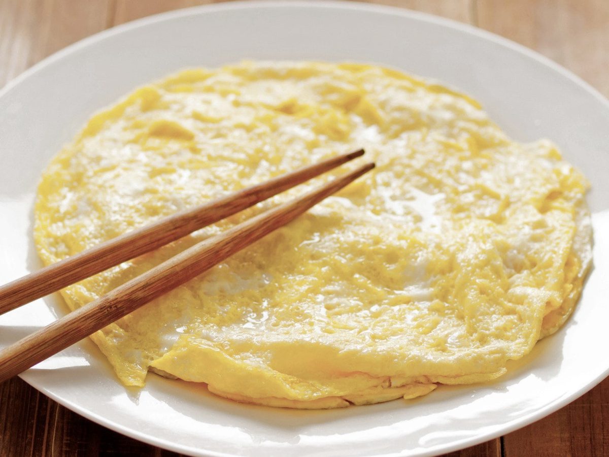 Mini Omeletts auf weißem Teller auf Holztisch mit Essstäbchen. Draufsicht.