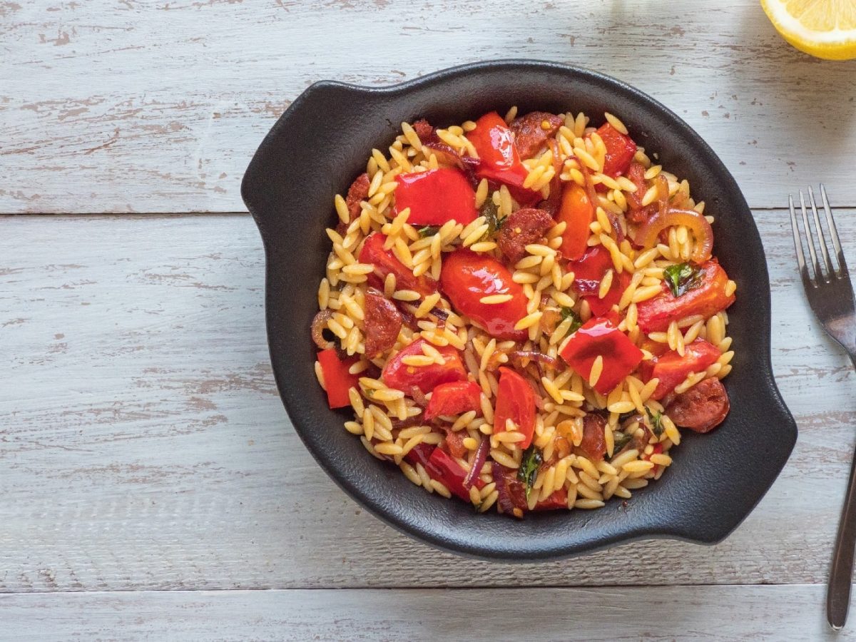 Ein schwarzer Topf mit der Chorizo-Pasta auf einem hellen Holztisch mit zwei Gabeln daneben.