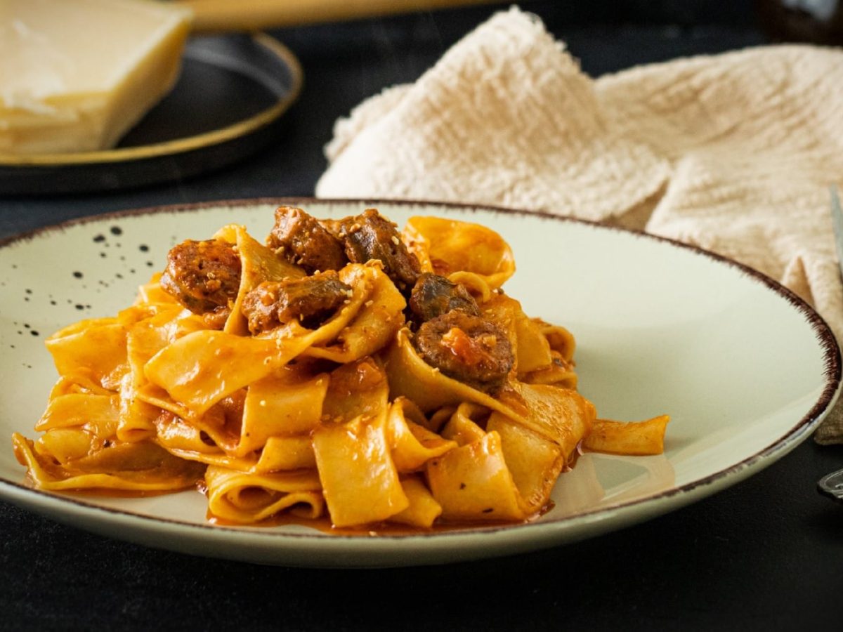 Ein grauer Teller mit der PAsta in roter Sauce und Wurst.