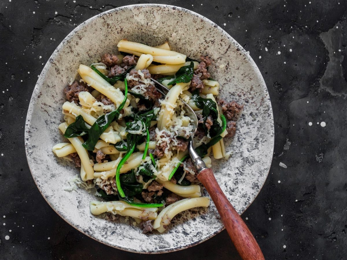 Ein grau-weiß-marmorierter Teller mit der Pasta auf einem dunkelgrauen Untergrund von oben fotografiert.