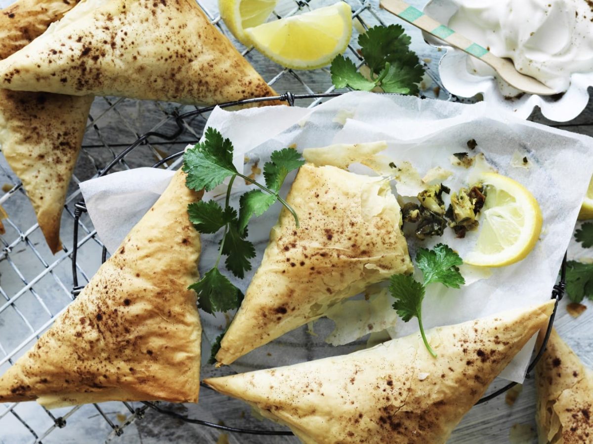 Einige Pastilla-Dreiecke mit Blumenkohl garniert mit Zitrone und Petersilie auf einem Gitter vor hellem Hintergrund.