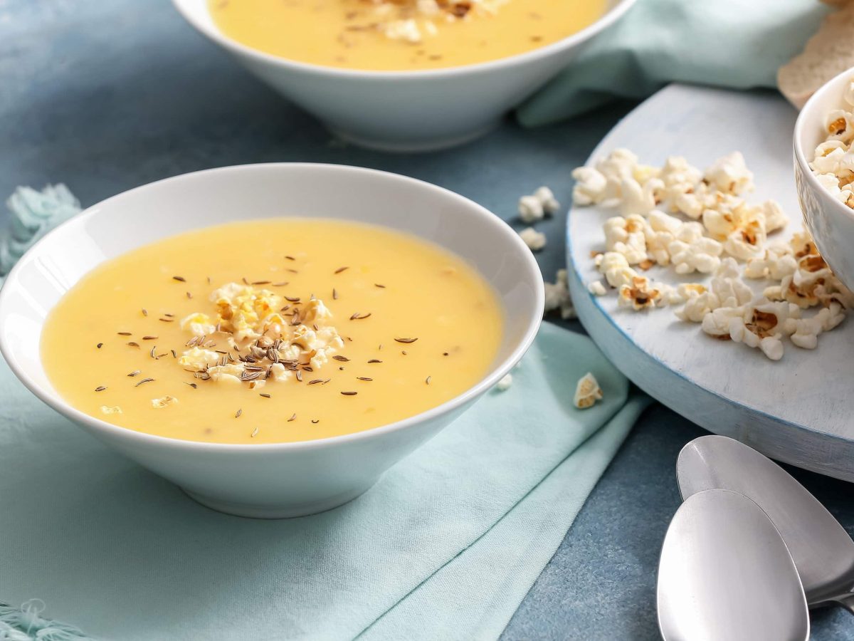 Zwei weiße Schalen mit der Popcorn-Suppe auf einem blauen Tischtuch. udn einer großen Schale mit Popcorn.