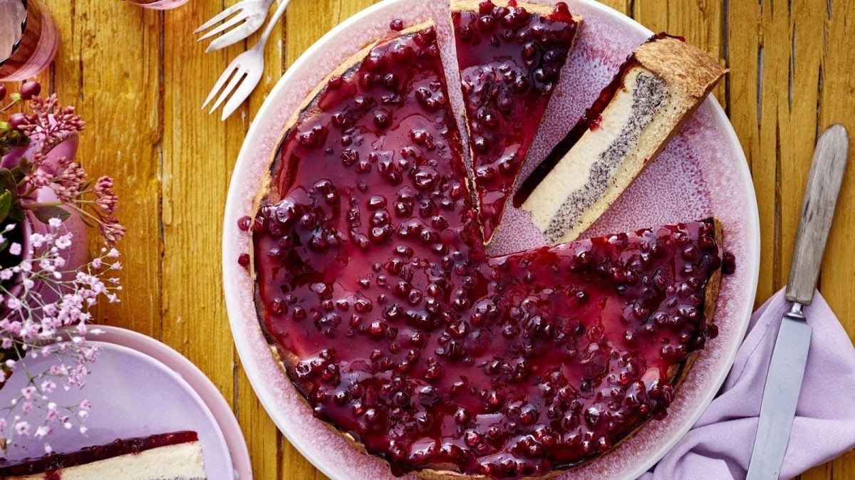 Draufsicht: Angeschnittener Preiselbeer-Mohn-Käsekuchen auf einem rosa Teller.