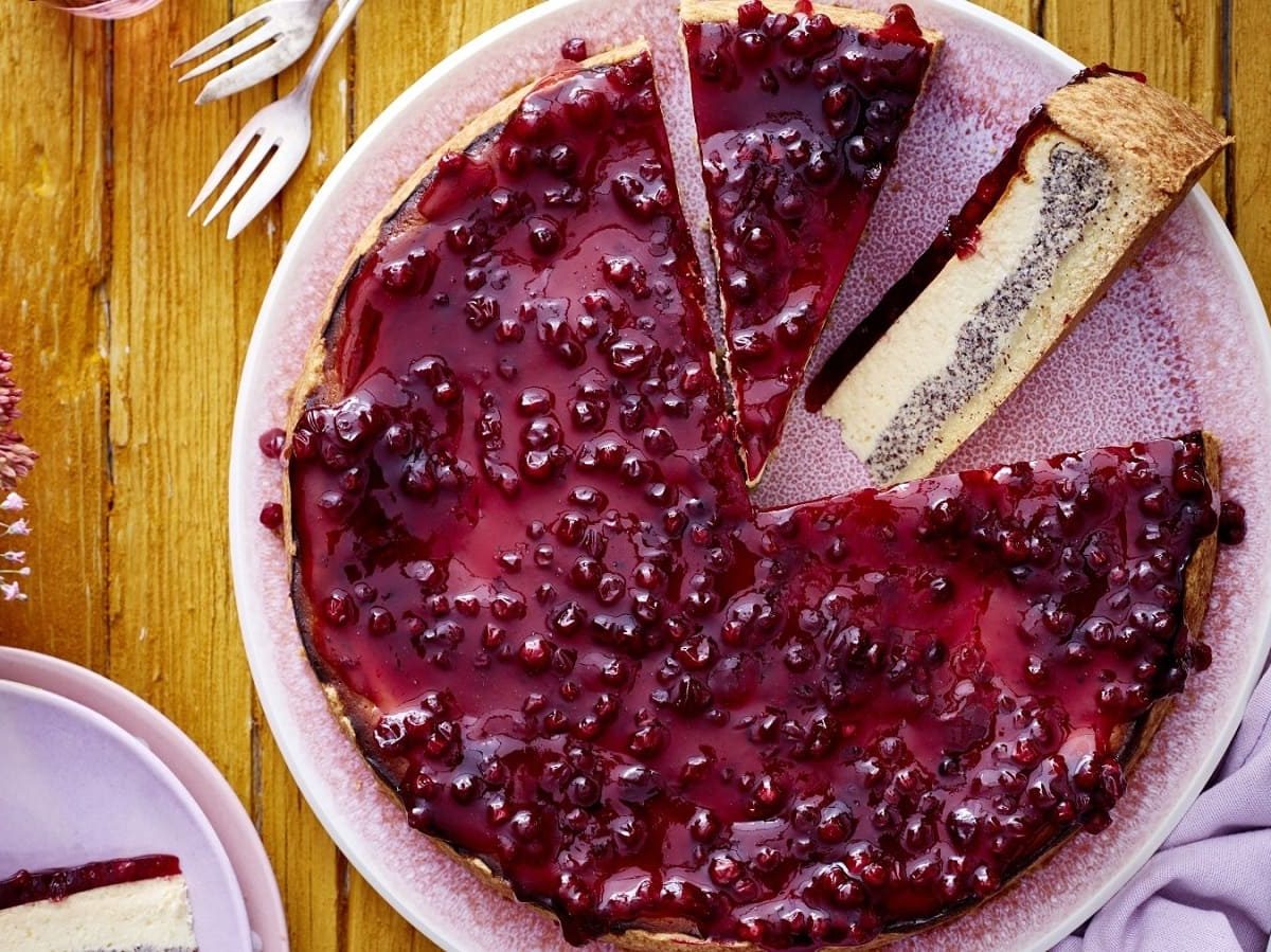 Draufsicht: Angeschnittener Preiselbeer-Mohn-Käsekuchen auf einem rosa Teller.