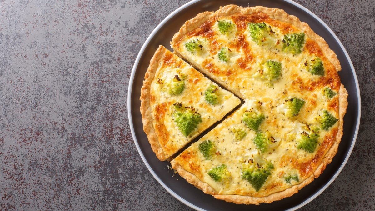 Ein angeschnittenes Stück aus der Romanesco-Quiche auf einem grauen Untergrund, direkt von oben fotografiert.