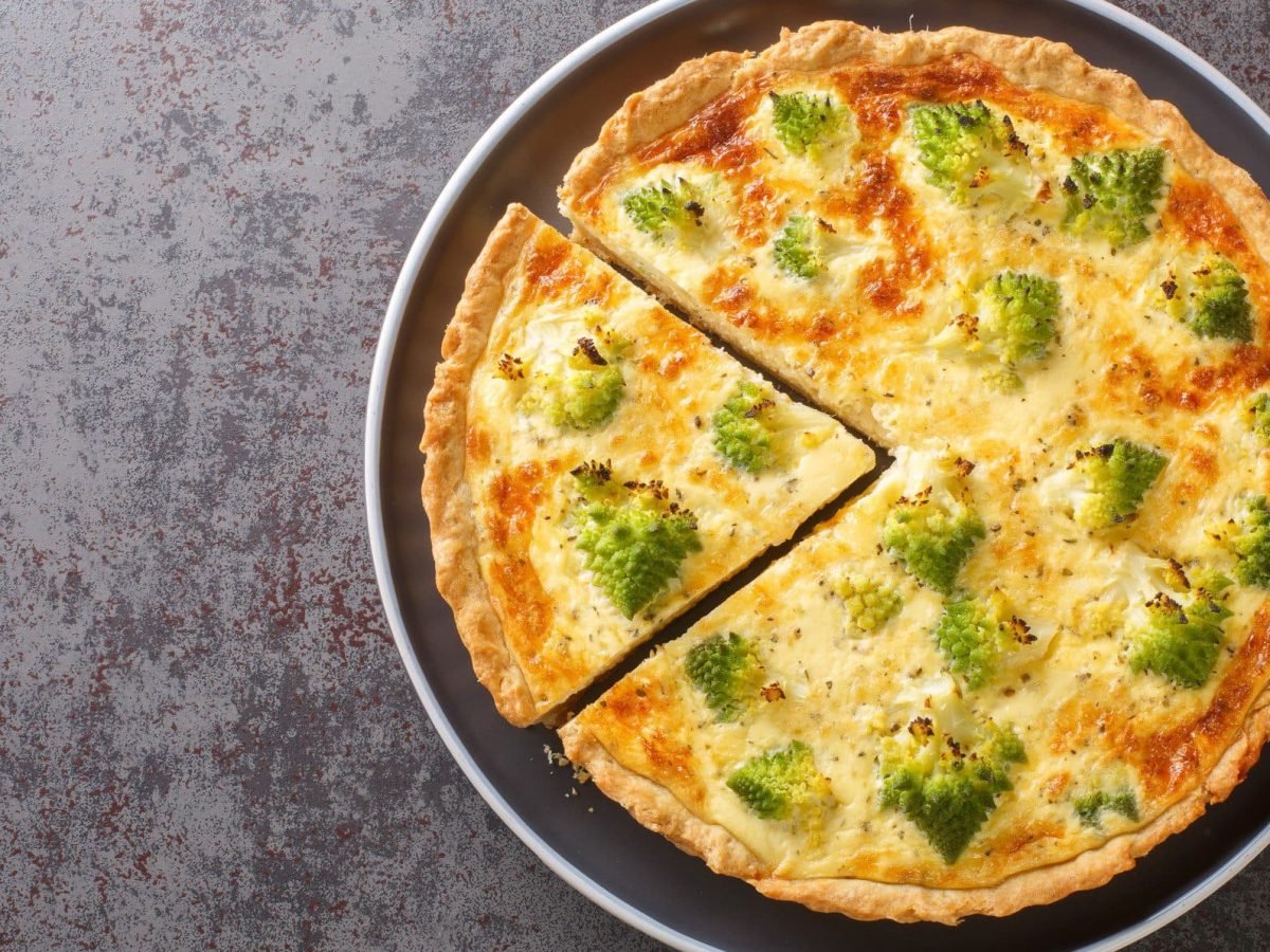 Ein angeschnittenes Stück aus der Romanesco-Quiche auf einem grauen Untergrund, direkt von oben fotografiert.