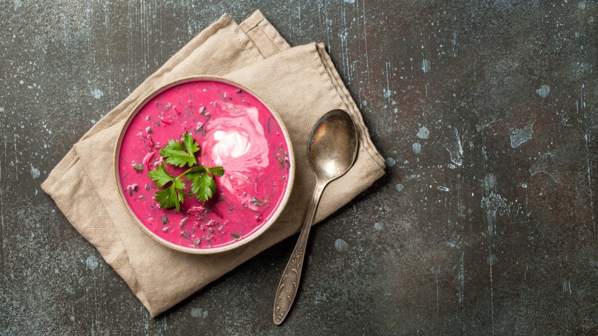 Rote-Bete-Cremesuppe mit Kokosmilch in einer Schüssel mit Löffel auf einem Tuch vor dunklem Hintergrund.