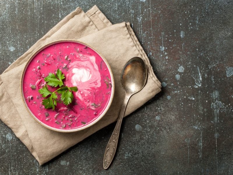 Rote-Bete-Cremesuppe mit Kokosmilch in einer Schüssel mit Löffel auf einem Tuch vor dunklem Hintergrund.