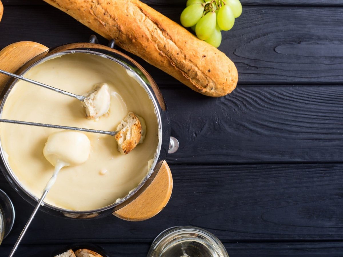 Ein Topf schnelles veganes Käsefondue mit Spießen, Weintrauben und Baguette in der Draufsicht.