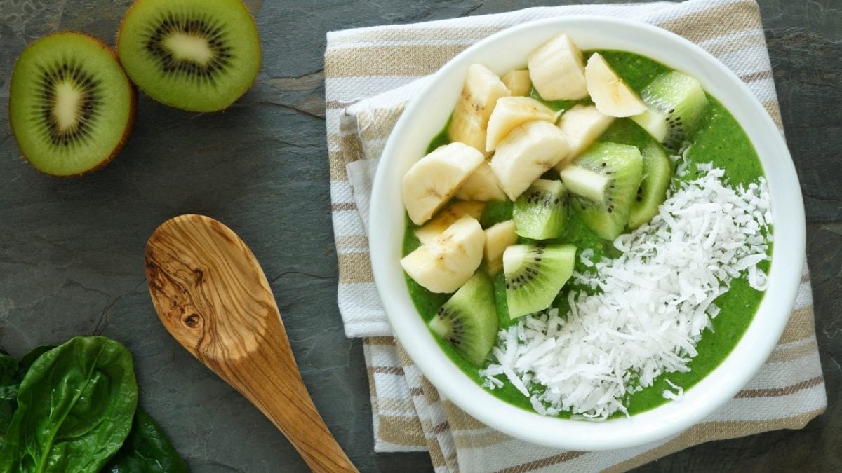 Draufblick: Eine Smoothie-Schüssel mit Spinat mit Kokosraspeln, Banane und Kiwi