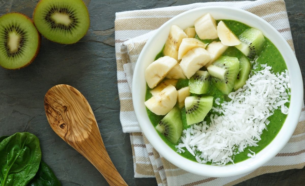 Draufblick: Eine Smoothie-Schüssel mit Spinat mit Kokosraspeln, Banane und Kiwi