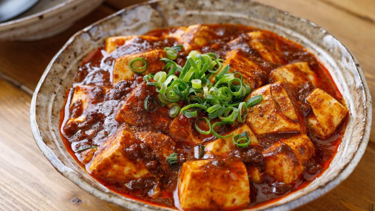 Eine Schüssel süß-saurer Chili-Tofu mit Frühlingszwiebeln in roter Sauce.