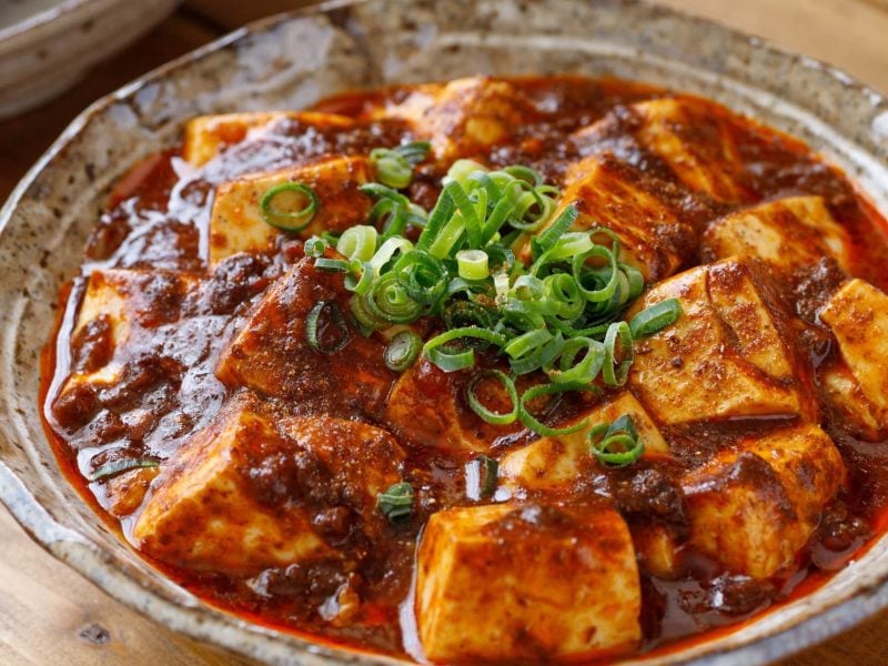 Eine Schüssel süß-saurer Chili-Tofu mit Frühlingszwiebeln in roter Sauce.