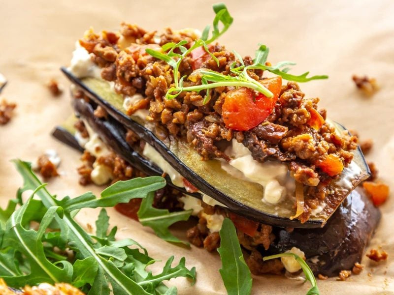 Ein Stück vegane Auberginen-Lasagne mit Linsen-Bolognese und Ruccola.