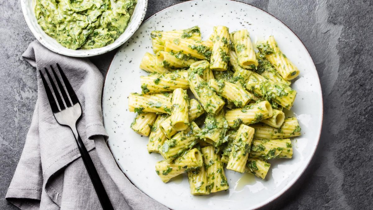 Ein Teller vegane Brokkoli-Pasta in der Draufsicht, daneben eine Gabel, eine Serviette und ein Teller mit noch mehr Nudeln.