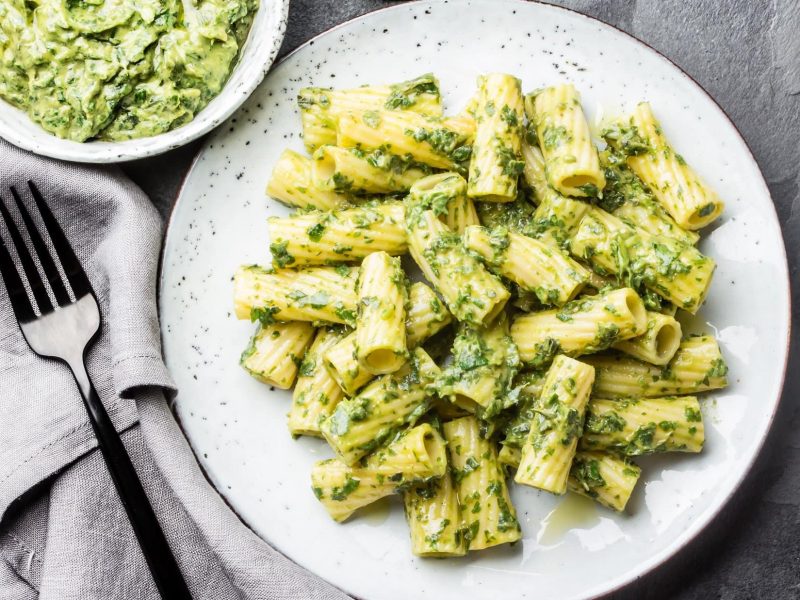 Ein Teller vegane Brokkoli-Pasta in der Draufsicht, daneben eine Gabel, eine Serviette und ein Teller mit noch mehr Nudeln.