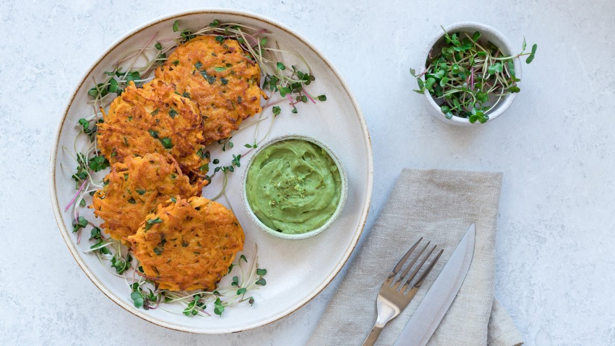 Ein Teller Kürbis-Frikadellen mit einer Schale Guacamole und Kresse, alles Draufsicht.