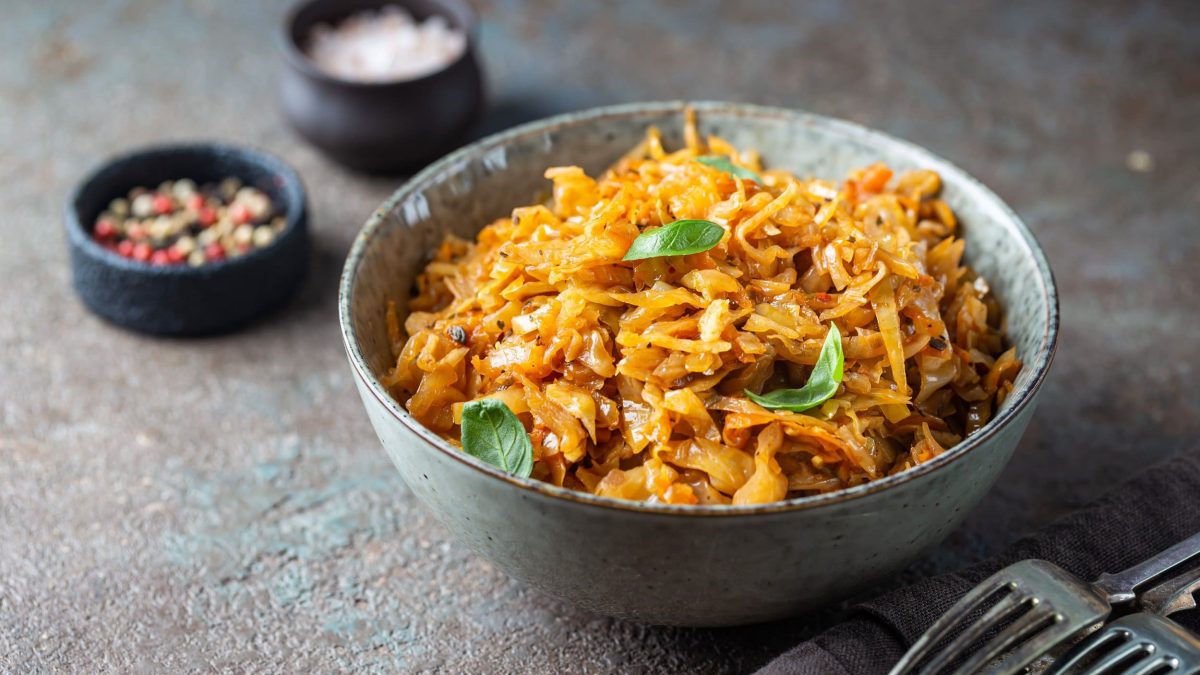 Eine Schüssel veganer Schmorkohl mit Basilikum, daneben Gabeln und Schälchen mit Gewürzen.