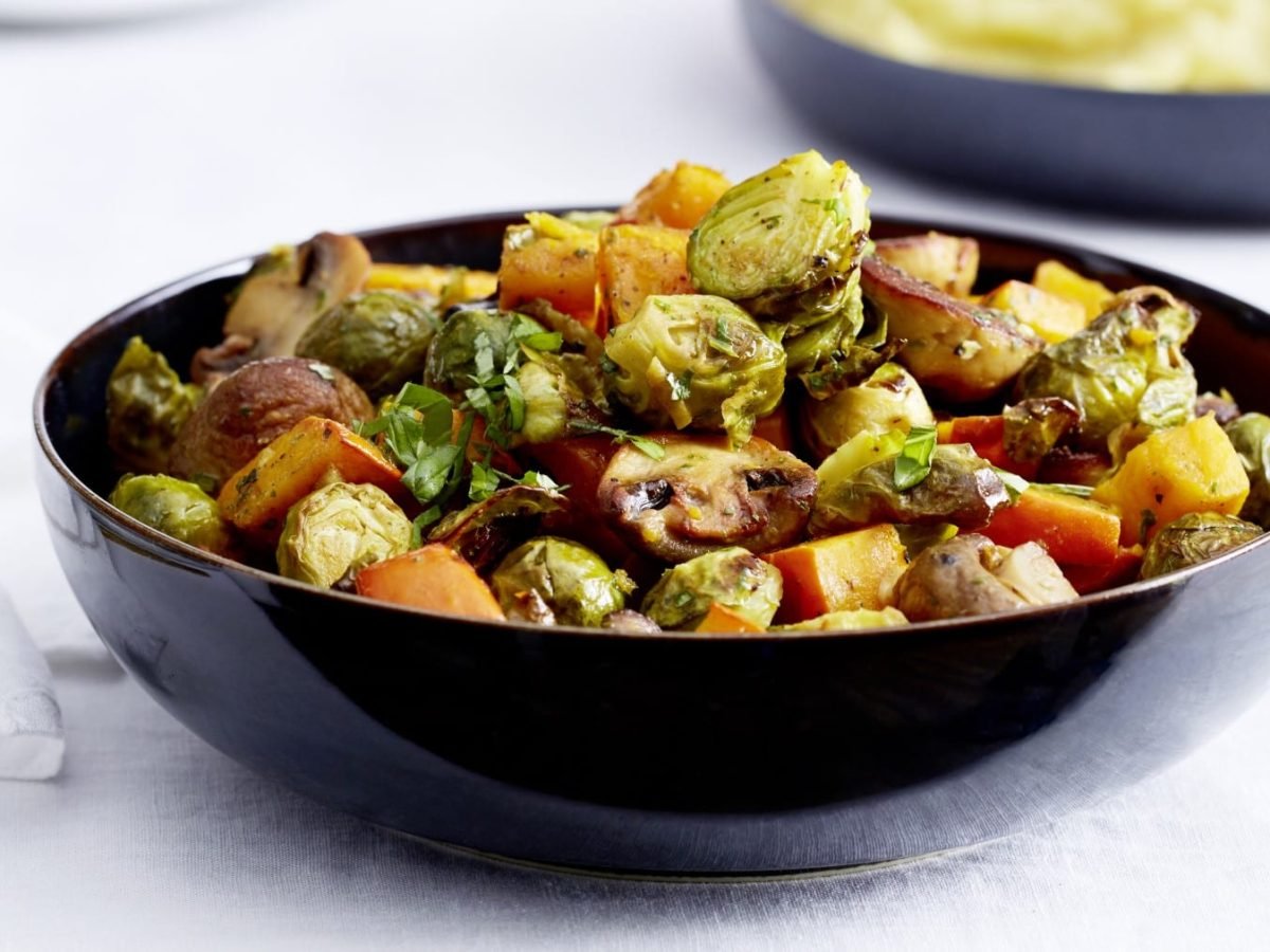 Warmer Röstgemüse-Salat in einer schwarzen Schüssel vor hellem Hintergrund.