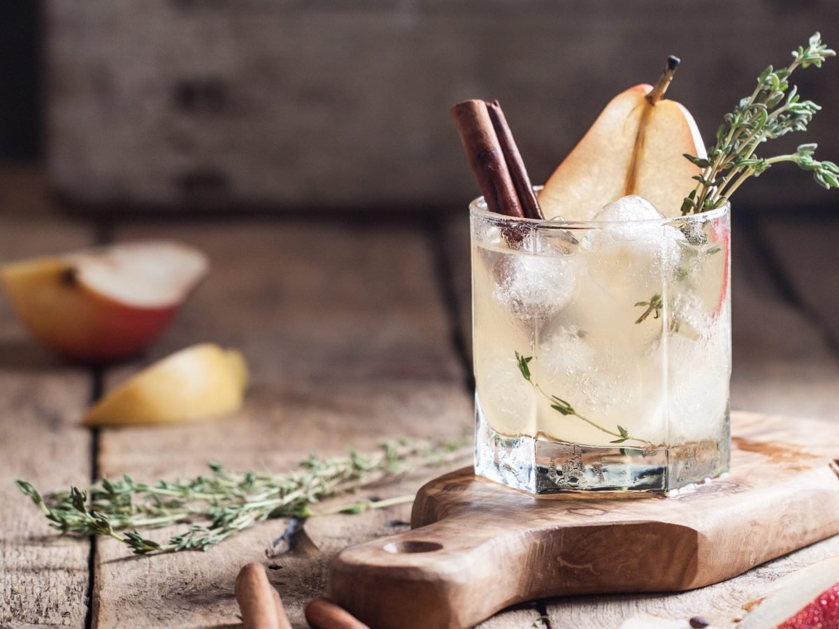 Ein Glas winterlicher Gin Tonic mit Birnensaft und Zimt, Eiswürfeln und Thymian.