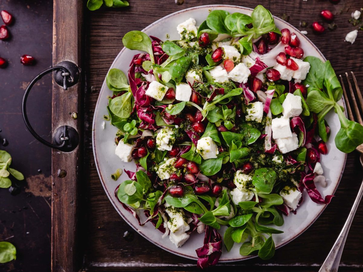 Draufsicht: Eine Wintersalat mit Radicchio, Feta und Granatapfel steht auf einem Tablettt. Daneben liegen zwei Gabeln aus Metall.