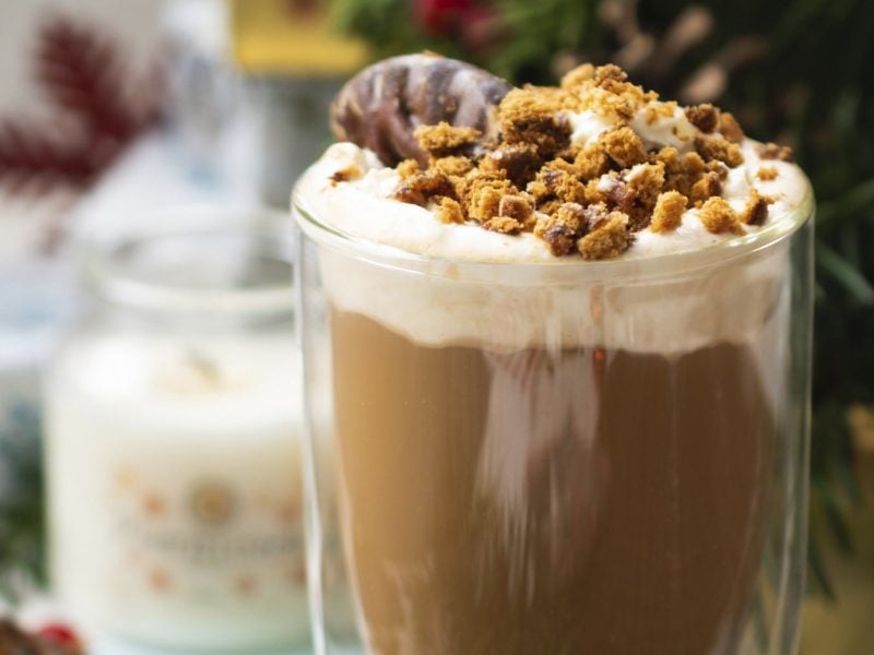 Lebkuchen-Latte mit Sahnehaube und Keks-Dekor, serviert in einem durchsichtigen Glas.