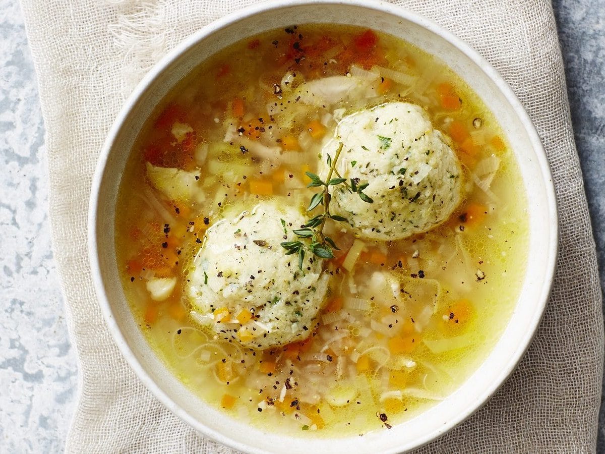 Draufsicht: eine weiße Schüssel mit einer klaren Suppe in der zwei Knödel sind.