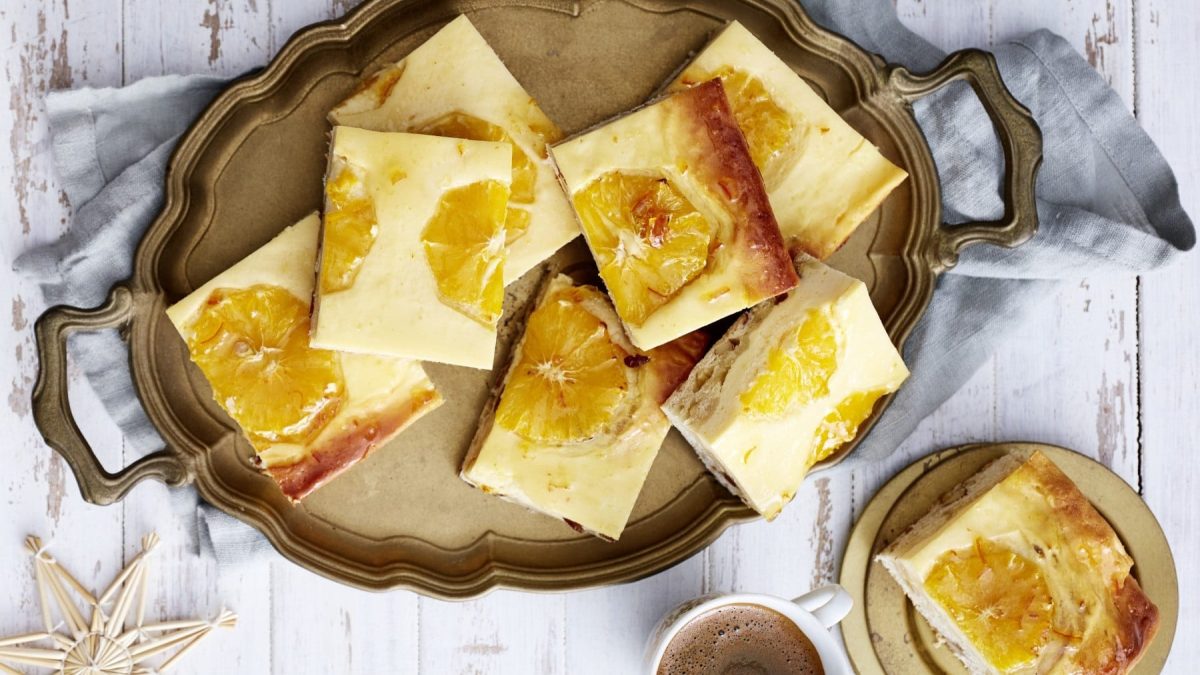 Stollen-Käseschnitten mit Orangenscheiben, serviert aufeinander gestapelt auf einem Servicetablett auf einem weißen Tisch.