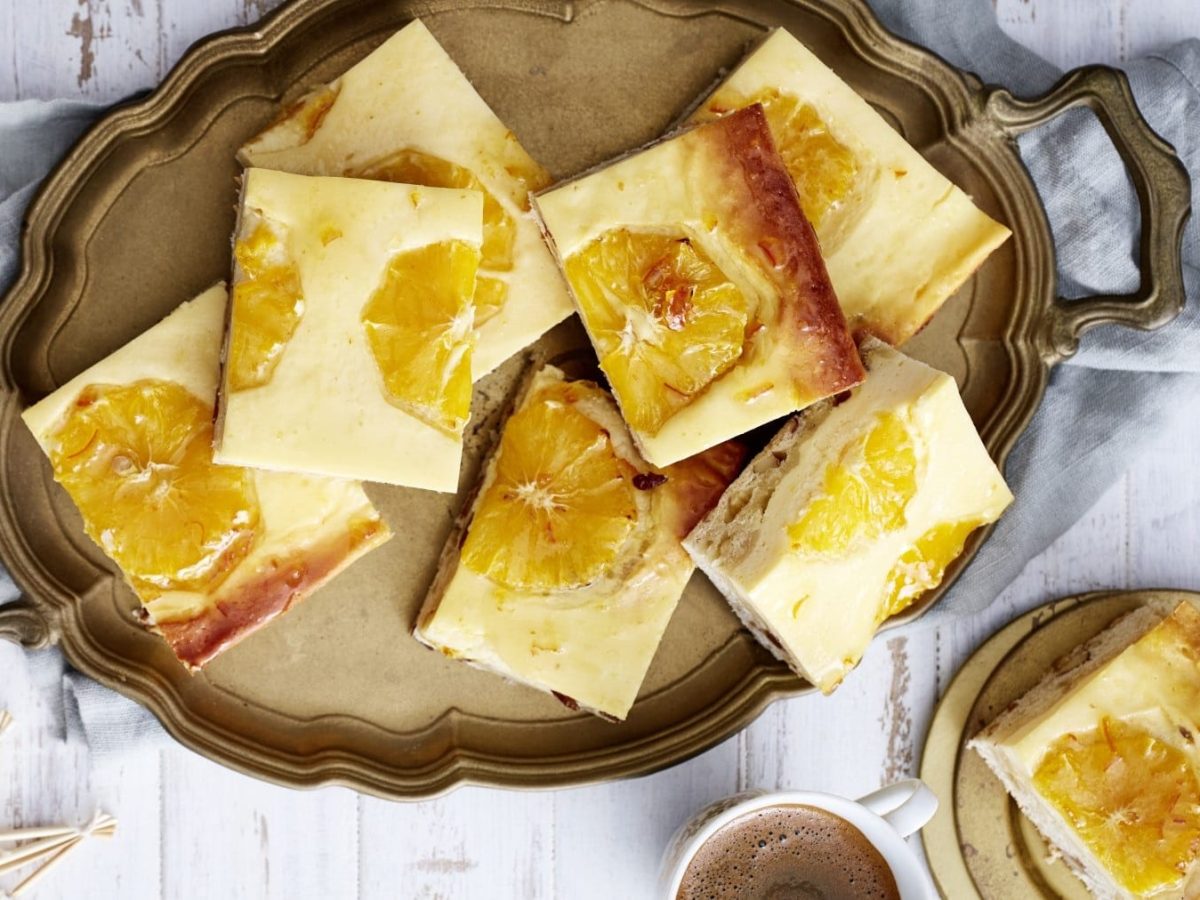 Stollen-Käseschnitten mit Orangenscheiben, serviert aufeinander gestapelt auf einem Servicetablett auf einem weißen Tisch.