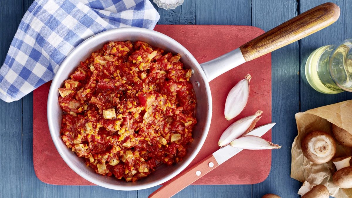 Tomaten-Pilz-Ragout, garniert mit Paprika und Chili und serviert auf einem Holzbrett in einem großen Topf