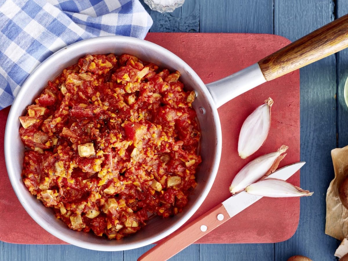 Tomaten-Pilz-Ragout, garniert mit Paprika und Chili und serviert auf einem Holzbrett in einem großen Topf