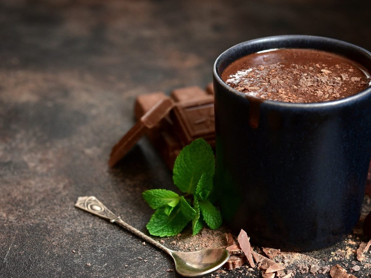 Ein Becher After Eight Hot Chocolate, daneben gekrümelte Schokolade, Minze und ein Löffel.