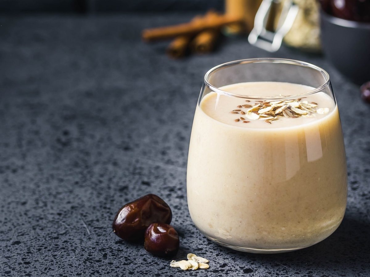 Ein Glas mit dem Bananen-Mate-Smoothie auf einem dunkelblauem Untergrund mit Datteln.