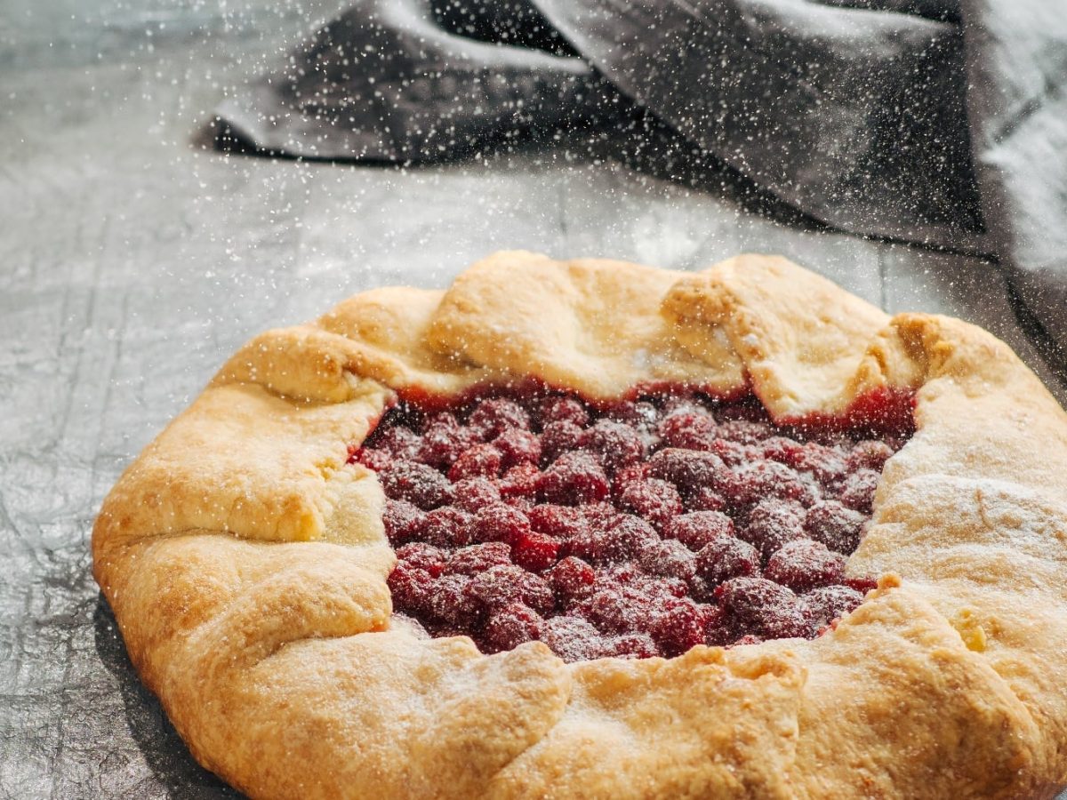 Die Galette mit Cranberrys auf einem grauen Untergrund. Die gAlette wird mit Puderzucker bestäubt.