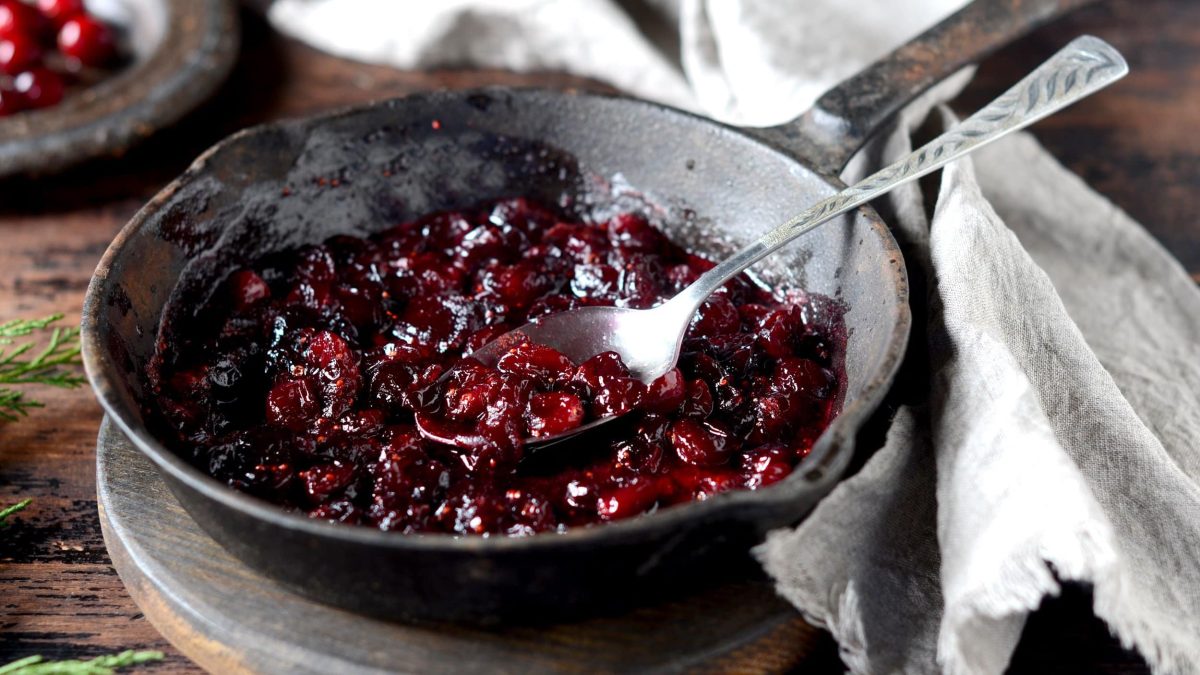 Eine gusseiserne Pfanne mit Cranberry-Kompott und einem Löffel.