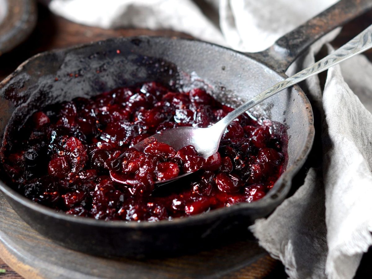 Eine gusseiserne Pfanne mit Cranberry-Kompott und einem Löffel.