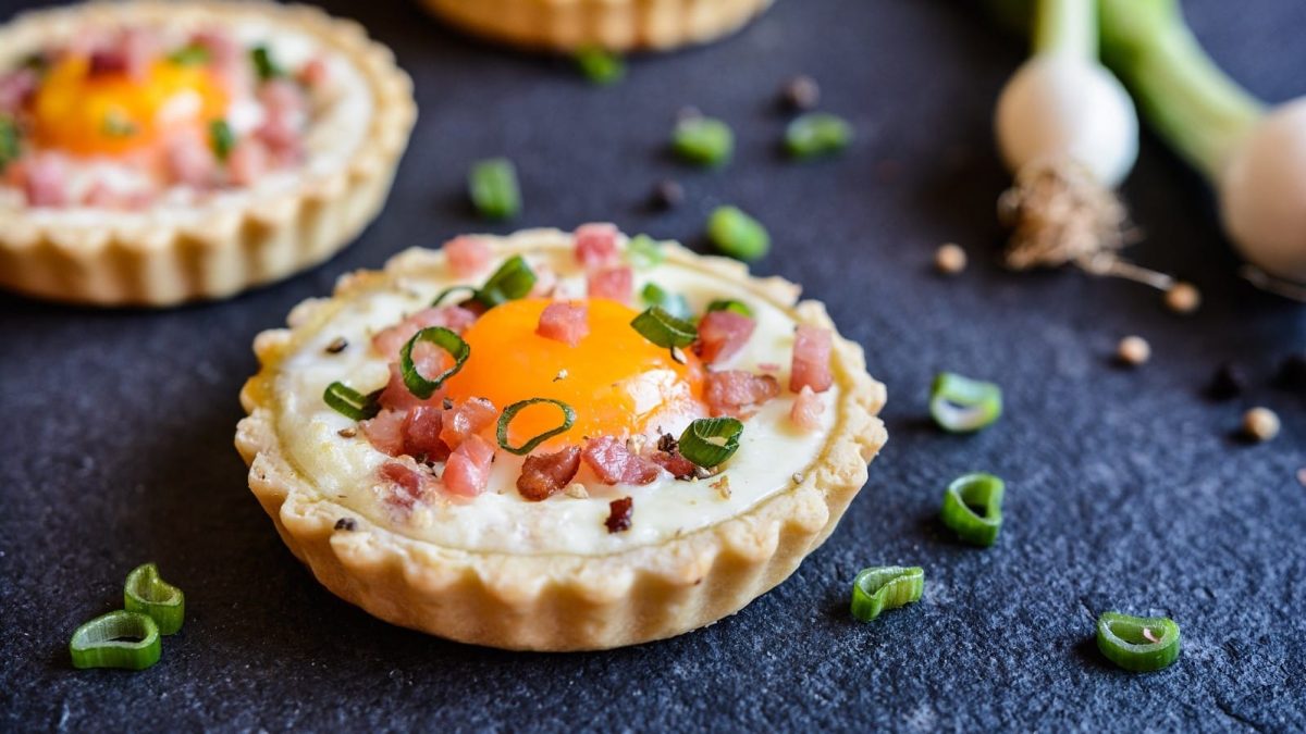 Mehrere Bacon-Ei-Tartelettes vor dunklem Hintergrund