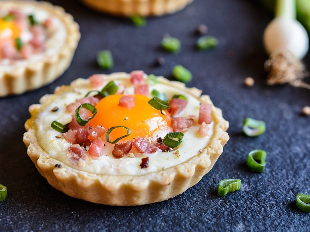 Mehrere Bacon-Ei-Tartelettes vor dunklem Hintergrund