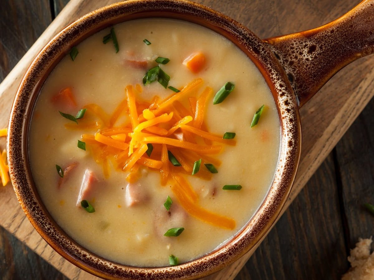 Eine braune Schüssel mit Bier-Käse-Suppe auf einem Holzbrett.