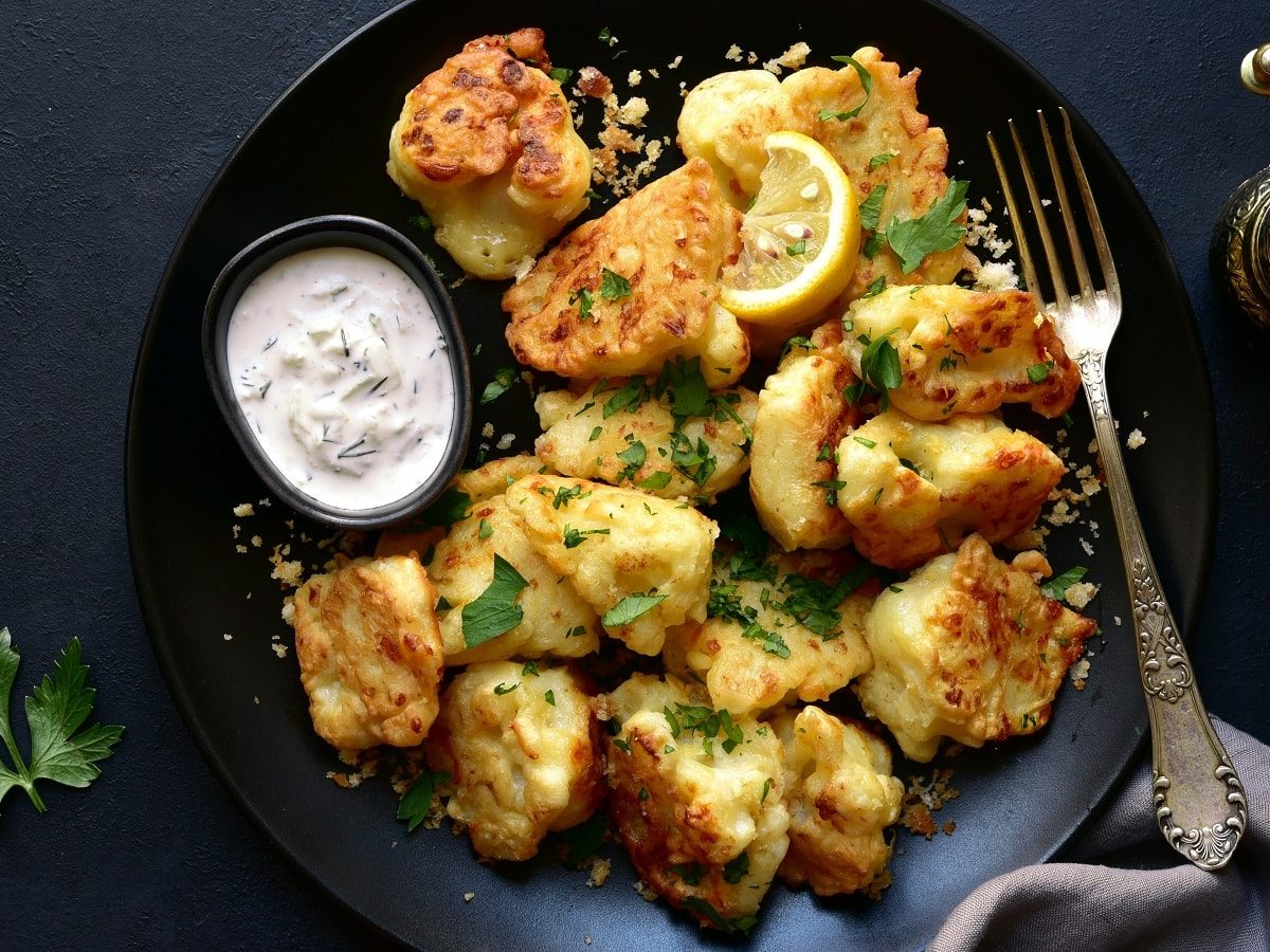 Ein schwarzer Teller mit Blumenkohl-Nuggets mit Käse.