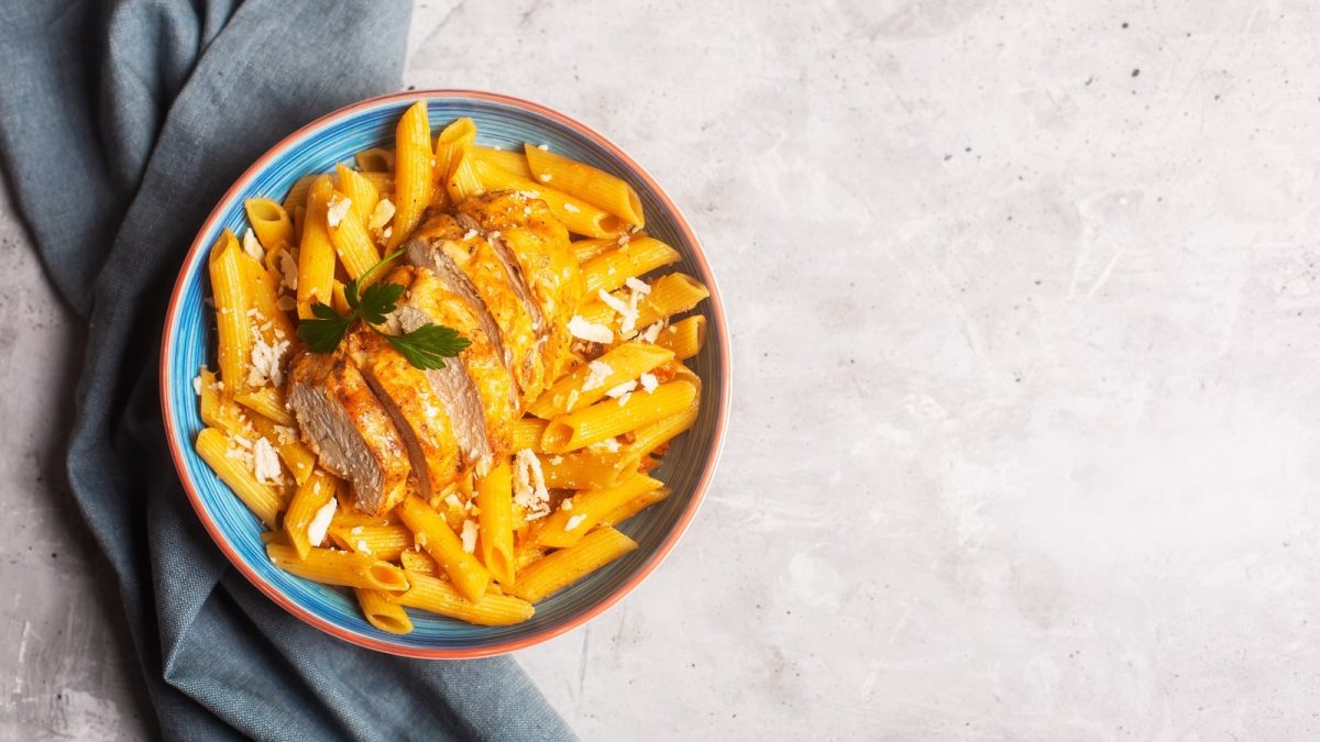 Ein blauer Teller mit Cajun Chicken Pasta auf einem hellen Tisch.