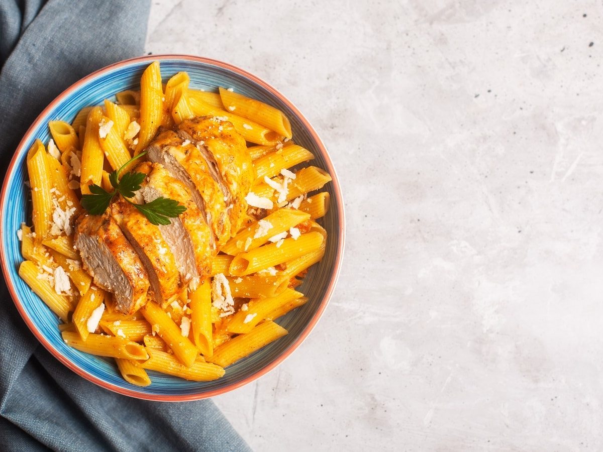 Ein blauer Teller mit Cajun Chicken Pasta auf einem hellen Tisch.