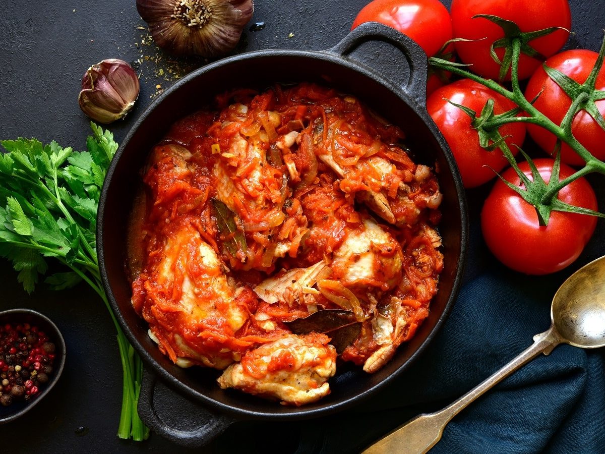 Ein schwarzer Topf mit Chakhokhbili auf einem schwarzen Tisch neben frischen Tomaten