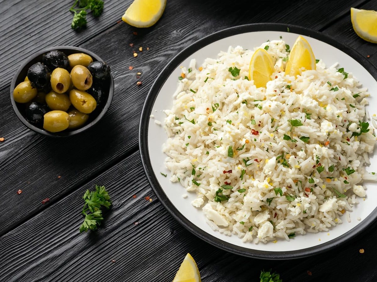 Ein weißer Teller mit Feta-Reis mit Zitrone auf einem dunklen Tisch.